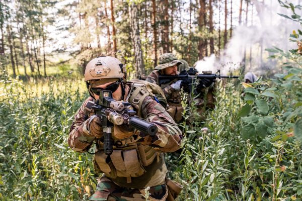 Group of soldiers in uniform moving through forest bushes while performing military reconnaissance operation