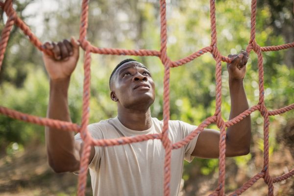 Military soldier climbing net during obstacle course in boot camp